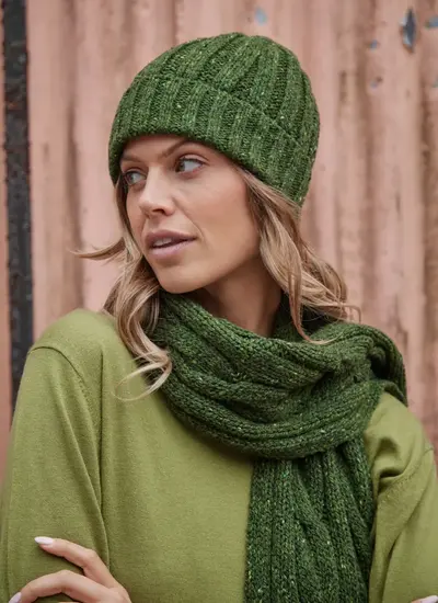 Woman wearing a ribbed Fisherman Donegal fleck beanie in shamrock green, styled with a matching cable knit scarf.